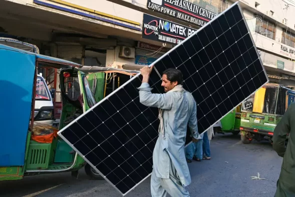 A worker carrying a solar panel at a market in Lahore, June 2024] Image Source: CNN, Photo By: Arif Ali/AFP/Getty Images