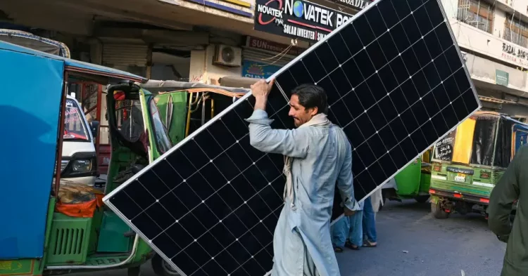 A worker carrying a solar panel at a market in Lahore, June 2024] Image Source: CNN, Photo By: Arif Ali/AFP/Getty Images