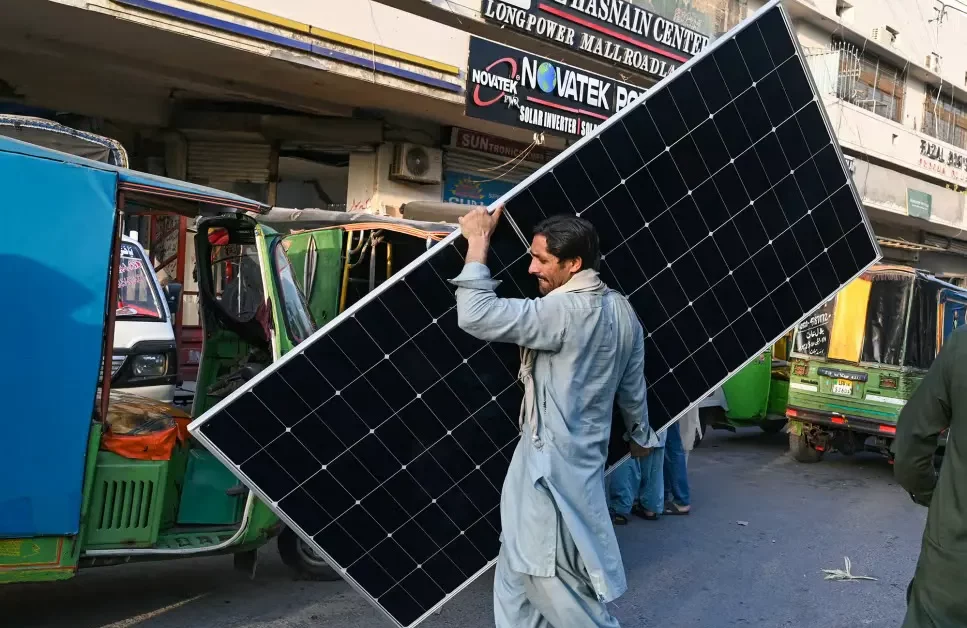 A worker carrying a solar panel at a market in Lahore, June 2024] Image Source: CNN, Photo By: Arif Ali/AFP/Getty Images