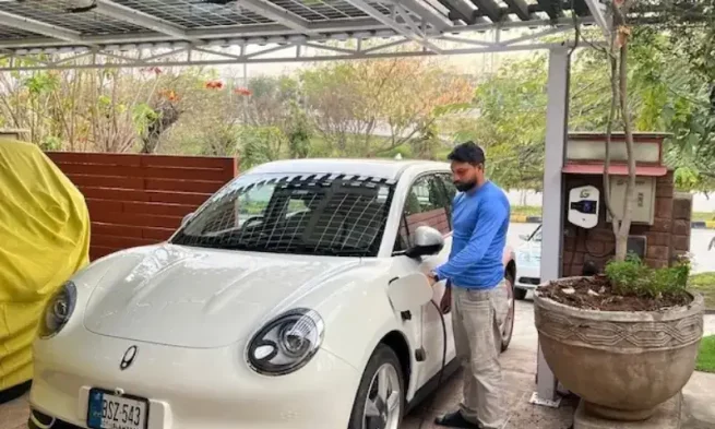 Vaqar Zakaria’s white EV charging under rooftop solar panels at his home in Islamabad] Image Source: Dawn